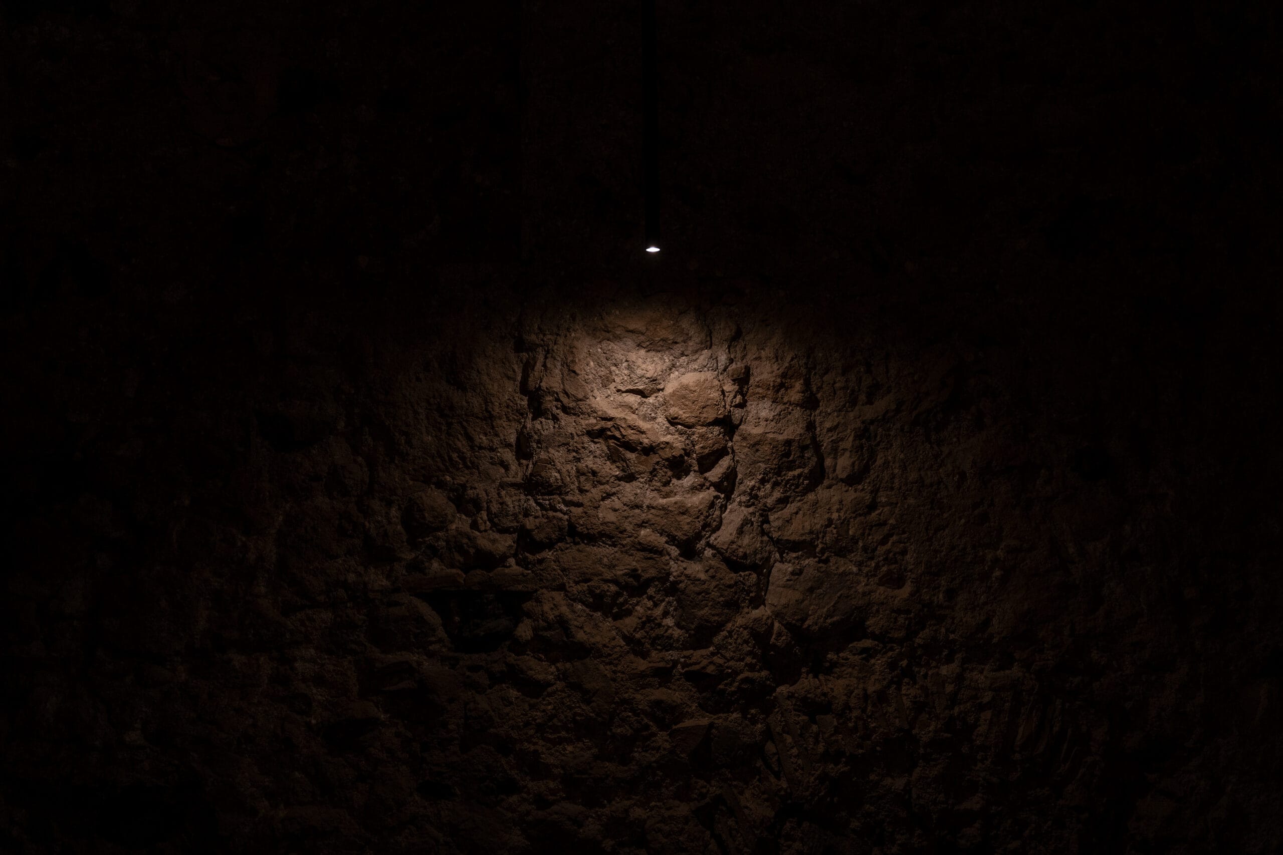 Un muro di pietra a vista illuminato da una sola lampada a sospensione, nel buio